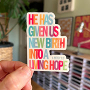 Eco-vinyl sticker with colorful text: 'He has given us new birth into a living hope' from 1 Peter 1:3.