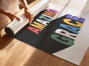 Colorful poster featuring the words 'AMAZING GRACE' in bold letters, being unrolled on a wooden surface.