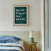 Botanical poster with the text 'Be still and know that I am God' in white on a green background, framed in wood.