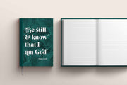 A5 hardback journal with a dark green cover featuring the text 'Be still & know that I am God' and a blank interior.