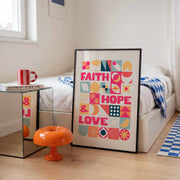 Colorful poster featuring the words 'Faith', 'Hope', and 'Love' in bold typography, displayed in a modern room.