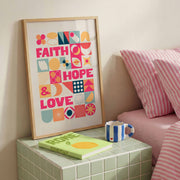 Poster featuring the words 'Faith Hope & Love' in colorful geometric designs, framed and displayed on a table.