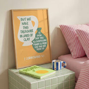 Poster featuring the text 'But we have this treasure in jars of clay' with a yellow mug illustration, framed in wood.