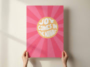 A person holding a pink A2 poster with the text 'Joy Comes In The Morning' in bold white letters, surrounded by sunburst