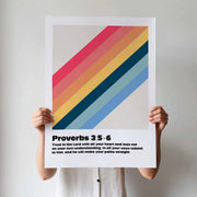 Colorful geometric wall art poster featuring Proverbs 3:5-6, held by a person with striped shirt.