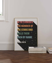 Christian wall art poster featuring Psalm 147:4 with colorful text on a starry background, framed on a wooden floor.