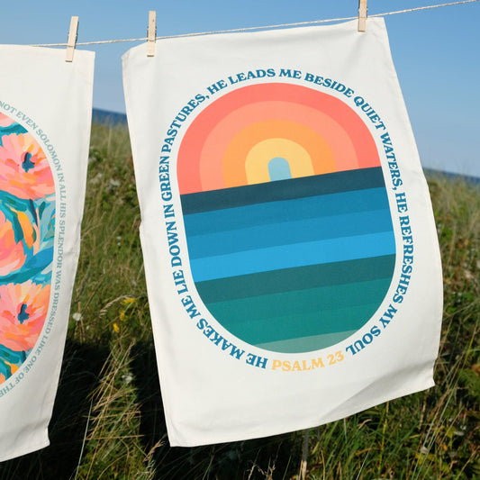 Decorative towel with a colorful design and bible text hanging on a clothesline outdoors.