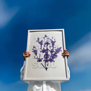 Framed poster with the text 'Then sings my soul' and purple flowers against a blue sky, held by a person.