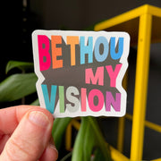 Colorful eco-vinyl sticker with the text 'BE THOU MY VISION' in bold letters, held against a dark background.