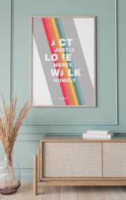 Poster featuring the text 'ACT JUSTLY, LOVE MERCY, WALK HUMBLE' in bold white letters with colorful stripes, framed and