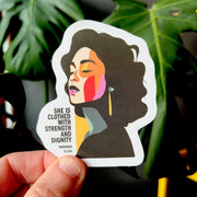 Eco-vinyl sticker featuring a woman with colorful abstract features and the text 'She is clothed with strength and dignity