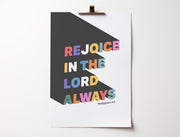 Poster featuring colorful text that reads 'Rejoice in the Lord always' with a modern design and Philippians 4:4 reference.