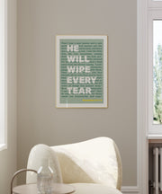 Framed poster with green text featuring the quote 'He will wipe every tear' on a light background, displayed on a wall.
