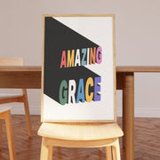 Poster featuring the text 'AMAZING GRACE' in colorful letters on a black background, displayed on a wooden chair.
