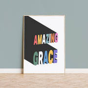 Poster featuring the text 'AMAZING GRACE' in colorful letters on a black background, framed and displayed on a wall.