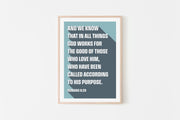 Poster featuring Romans 8:28 text in bold white font on a blue background, framed in light wood.