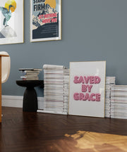 Neon effect poster with the text 'SAVED BY GRACE' displayed on a wall, surrounded by books and a table.