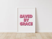 Neon effect poster with the text 'SAVED BY GRACE' in pink, framed and displayed on a white wall.